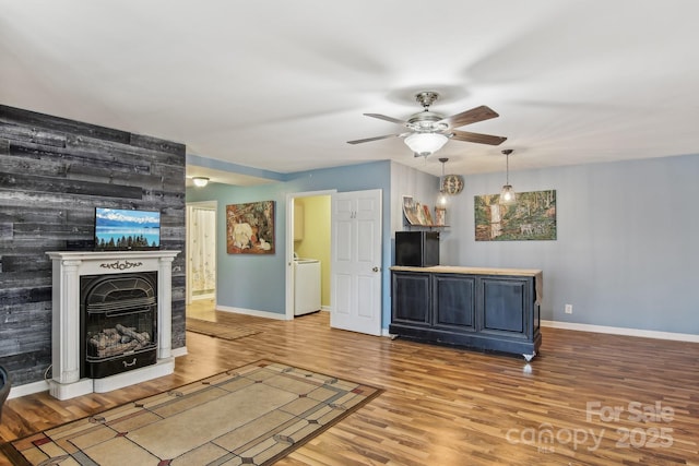 unfurnished living room with a fireplace, wood finished floors, washer / clothes dryer, baseboards, and ceiling fan