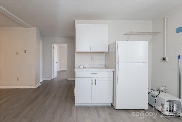 kitchen featuring light countertops, freestanding refrigerator, light wood finished floors, white cabinetry, and baseboards
