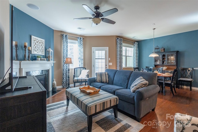 living area featuring wood finished floors, a premium fireplace, baseboards, visible vents, and ceiling fan