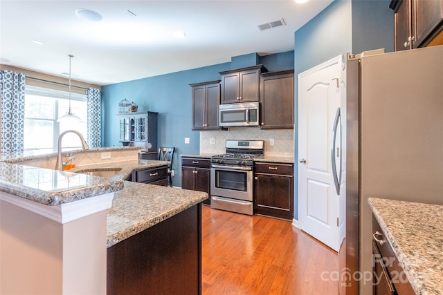 kitchen featuring a sink, backsplash, appliances with stainless steel finishes, light wood-style flooring, and visible vents