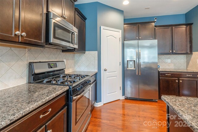 kitchen with stainless steel appliances, decorative backsplash, stone countertops, dark brown cabinetry, and wood finished floors