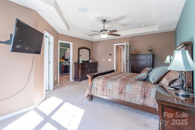 bedroom featuring a tray ceiling, light colored carpet, a closet, and a spacious closet