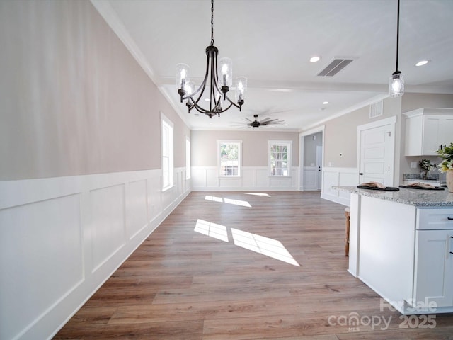 unfurnished dining area featuring light wood-type flooring, ornamental molding, ceiling fan with notable chandelier, and visible vents