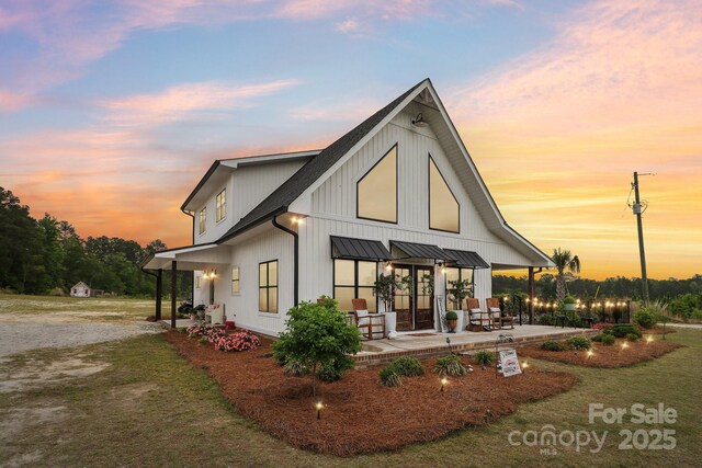 back of property at dusk with metal roof, a standing seam roof, a lawn, and a patio area