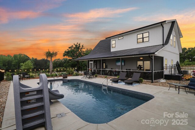 pool at dusk featuring fence, a sunroom, a patio, and a fenced in pool