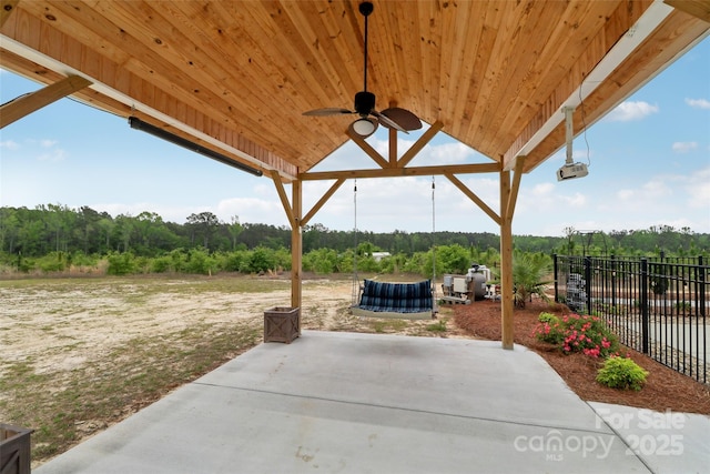 view of patio / terrace featuring a ceiling fan, fence, and a wooded view