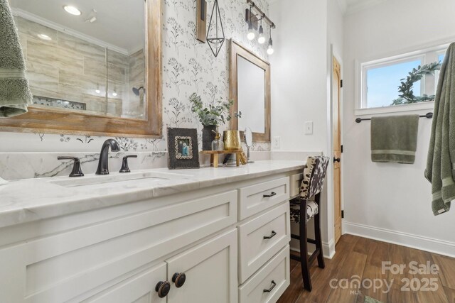 full bath with tiled shower, wood finished floors, vanity, baseboards, and crown molding