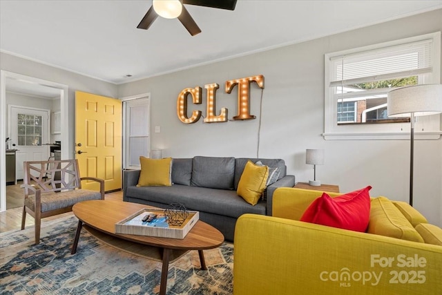 living area with a ceiling fan, ornamental molding, and wood finished floors