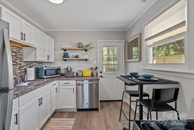 kitchen with crown molding, backsplash, light wood finished floors, appliances with stainless steel finishes, and white cabinets