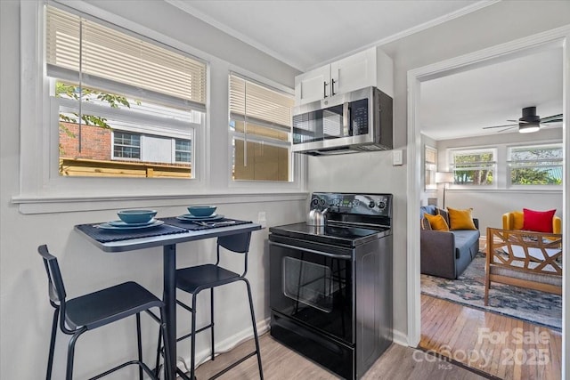 kitchen featuring white cabinetry, crown molding, stainless steel microwave, electric range, and wood finished floors