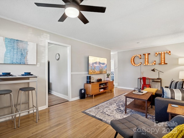living area with a ceiling fan, a textured ceiling, baseboards, and wood finished floors