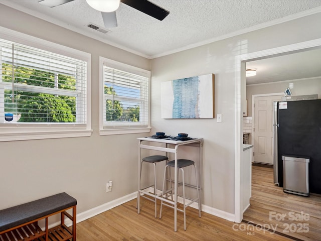 interior space with crown molding, light wood-style floors, ceiling fan, and visible vents