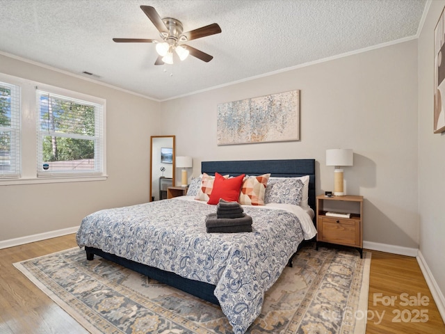 bedroom with wood finished floors, crown molding, baseboards, and visible vents