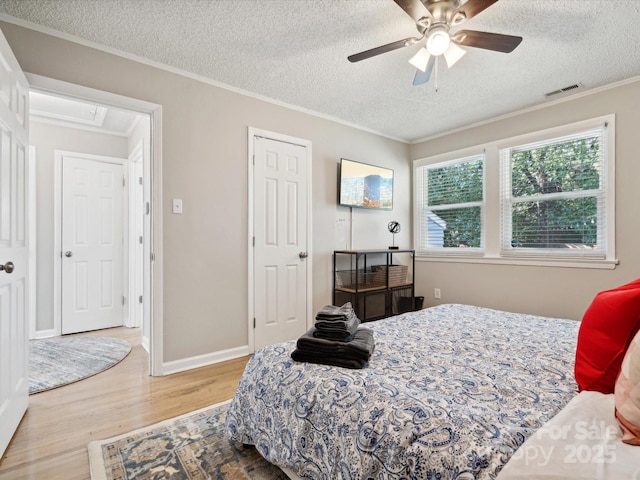 bedroom with ornamental molding, baseboards, a textured ceiling, visible vents, and wood finished floors