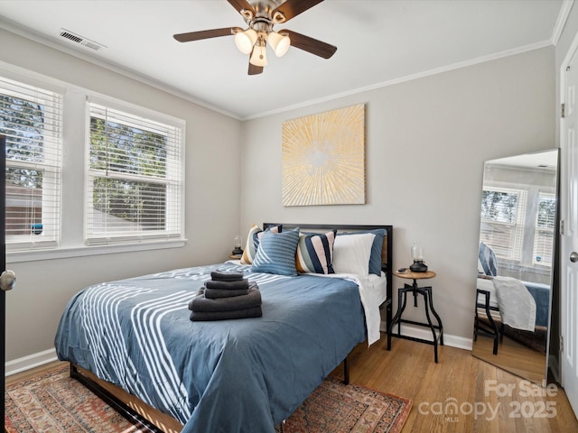 bedroom with baseboards, visible vents, crown molding, and wood finished floors
