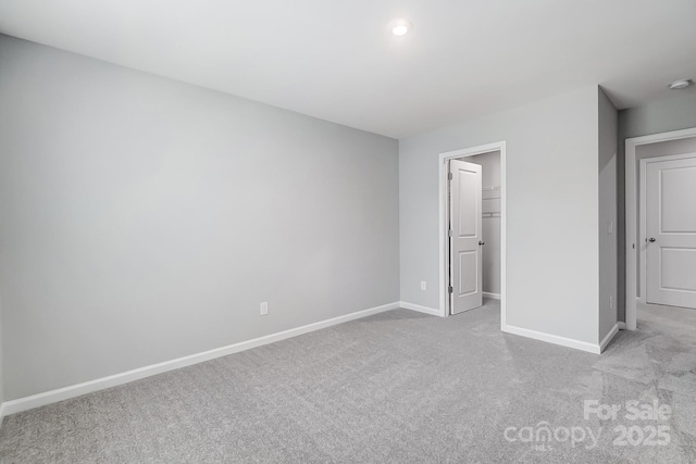 unfurnished bedroom with carpet floors, a walk in closet, and baseboards