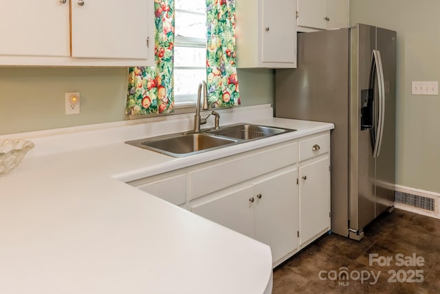kitchen with stainless steel fridge, light countertops, white cabinetry, visible vents, and a sink