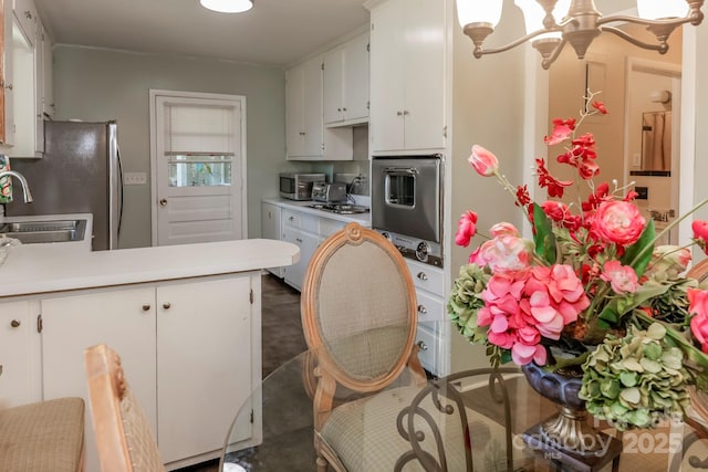 kitchen with a sink, light countertops, freestanding refrigerator, a peninsula, and white cabinetry