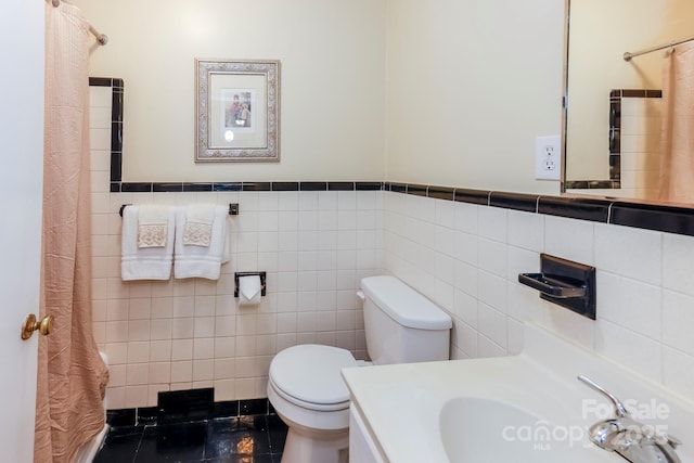 bathroom with a shower with shower curtain, tile walls, toilet, vanity, and wainscoting