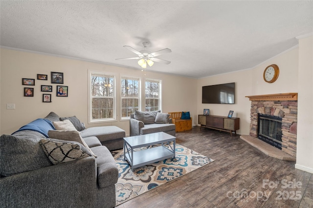 living area featuring crown molding, wood finished floors, a textured ceiling, a stone fireplace, and ceiling fan