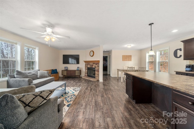 living area featuring a textured ceiling, dark wood finished floors, a stone fireplace, baseboards, and ceiling fan