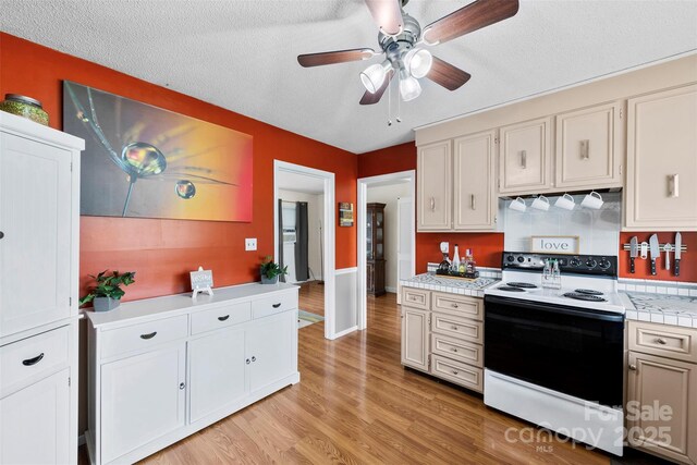 kitchen with a textured ceiling, light wood-type flooring, tile countertops, electric range, and ceiling fan