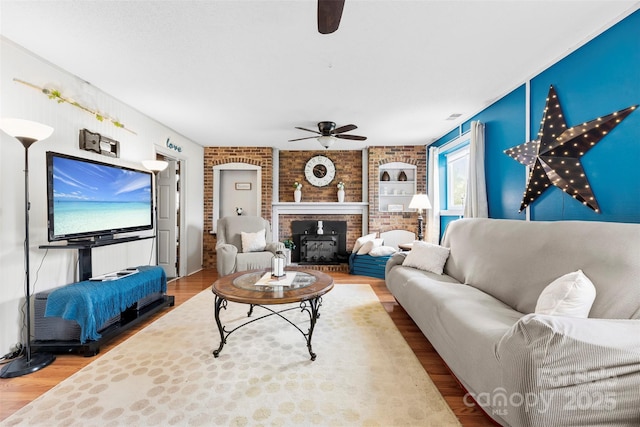 living area featuring visible vents, a brick fireplace, wood finished floors, a ceiling fan, and brick wall