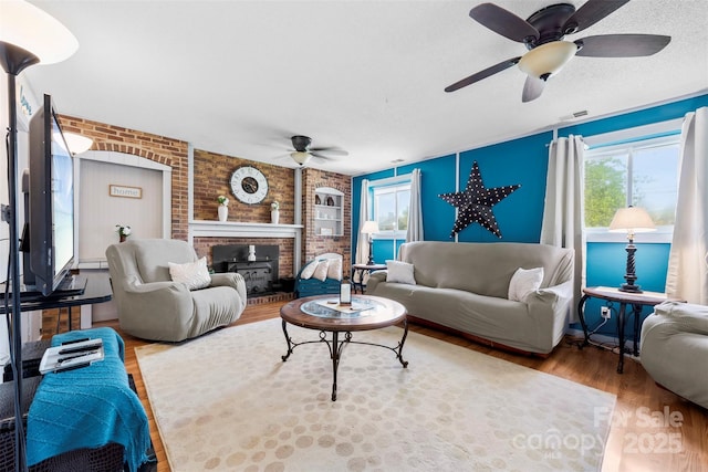 living room with visible vents, a fireplace, wood finished floors, a ceiling fan, and brick wall