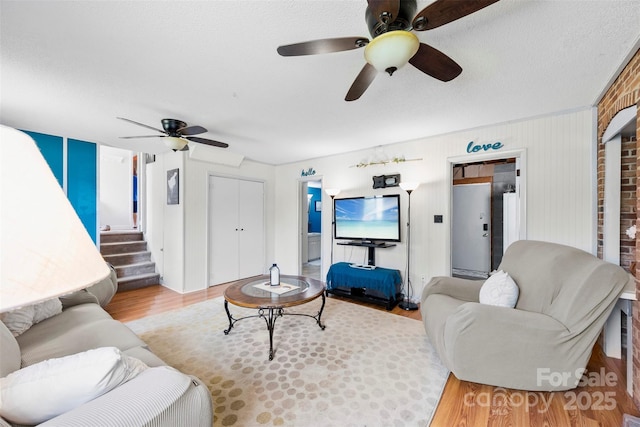 living area featuring a ceiling fan, light wood-style floors, stairs, and a textured ceiling