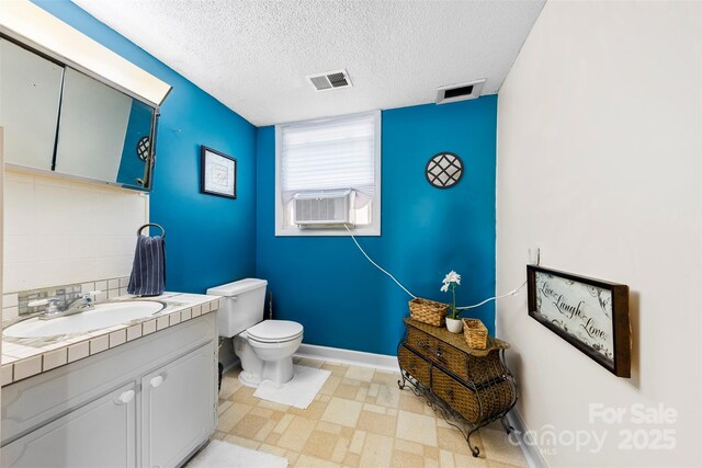 bathroom featuring toilet, vanity, cooling unit, a textured ceiling, and visible vents
