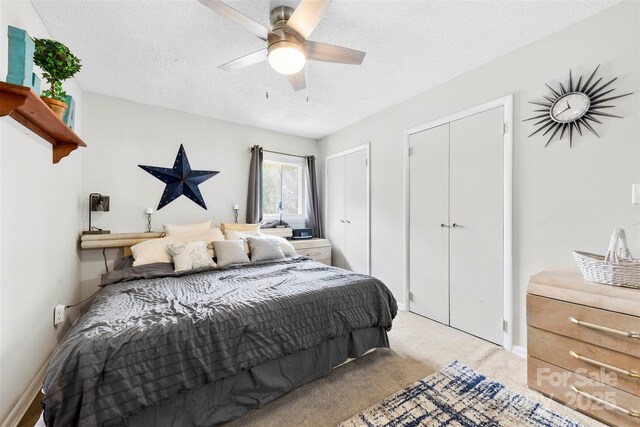 bedroom with two closets, light colored carpet, baseboards, a textured ceiling, and a ceiling fan