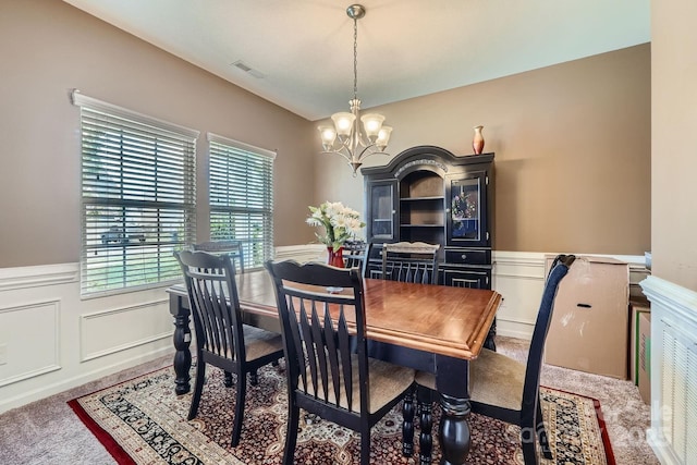 carpeted dining room featuring wainscoting, visible vents, a chandelier, and a decorative wall