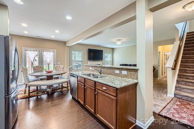 kitchen with stainless steel appliances, a sink, dark wood-style flooring, brown cabinets, and light stone countertops