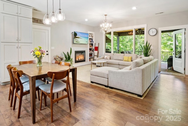 dining space featuring a chandelier, a glass covered fireplace, light wood-style floors, and recessed lighting
