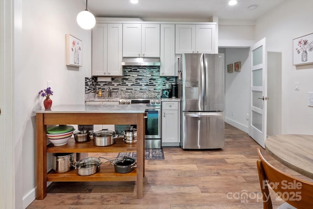 kitchen with appliances with stainless steel finishes, light countertops, under cabinet range hood, backsplash, and light wood-style floors
