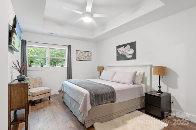 bedroom with a raised ceiling, hardwood / wood-style flooring, and baseboards