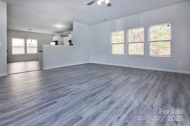 unfurnished living room with dark wood-type flooring, ceiling fan, and baseboards