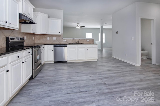 kitchen with a ceiling fan, dark countertops, a peninsula, under cabinet range hood, and stainless steel appliances