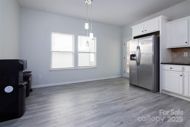kitchen with white cabinets, baseboards, stainless steel fridge, light wood finished floors, and backsplash
