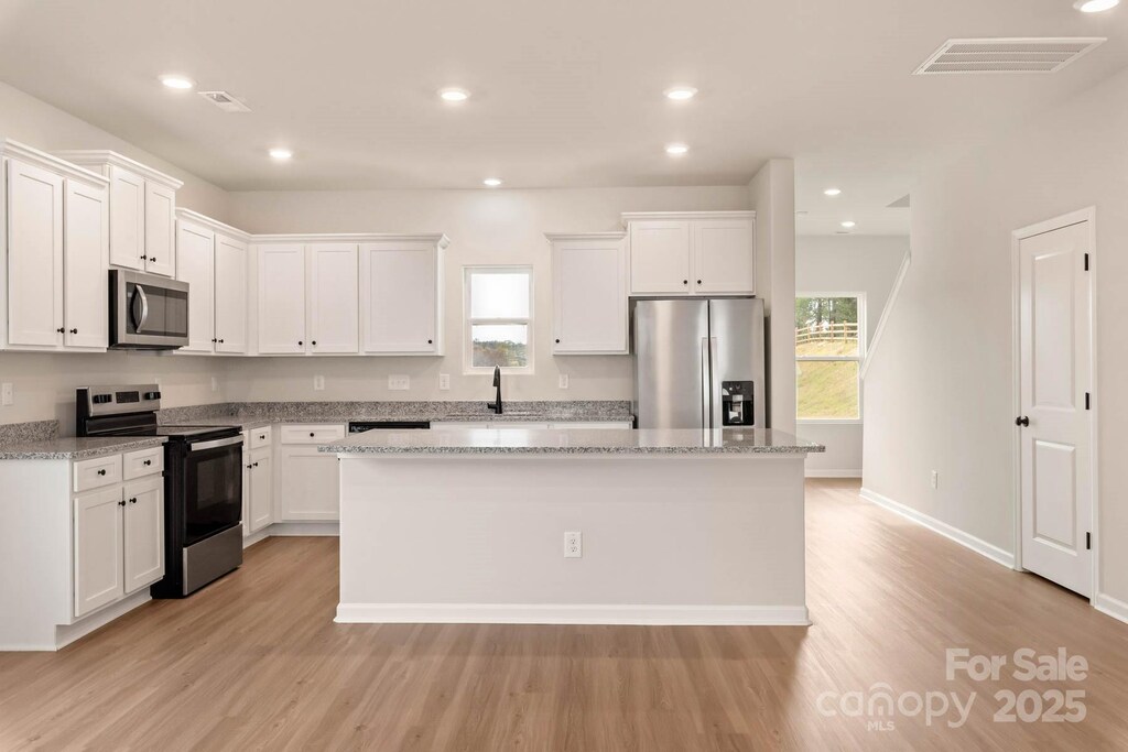 kitchen featuring a kitchen island, a sink, visible vents, white cabinets, and appliances with stainless steel finishes