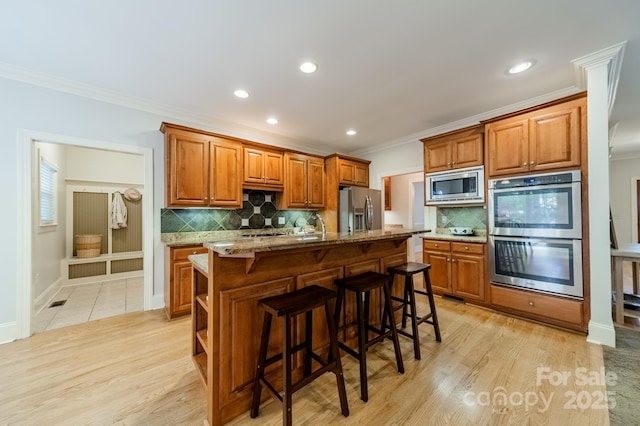 4599 Rustling Woods Dr, Denver, NC 28037 - kitchen with stainless steel appliances, brown cabinetry, crown molding, backsplash, and a breakfast bar area