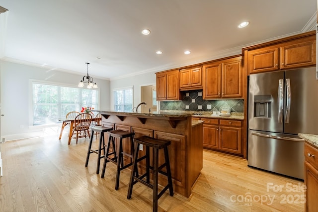 4599 Rustling Woods Dr, Denver, NC 28037 - kitchen featuring stainless steel fridge, ornamental molding, brown cabinets, light wood-style flooring, and a breakfast bar area