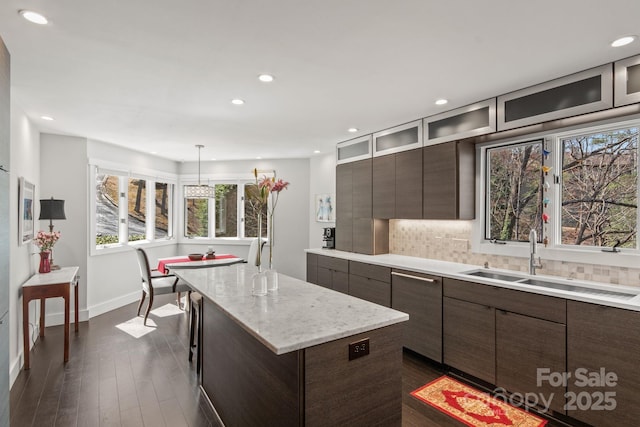 kitchen with backsplash, a kitchen island, a sink, glass insert cabinets, and dark wood-style flooring