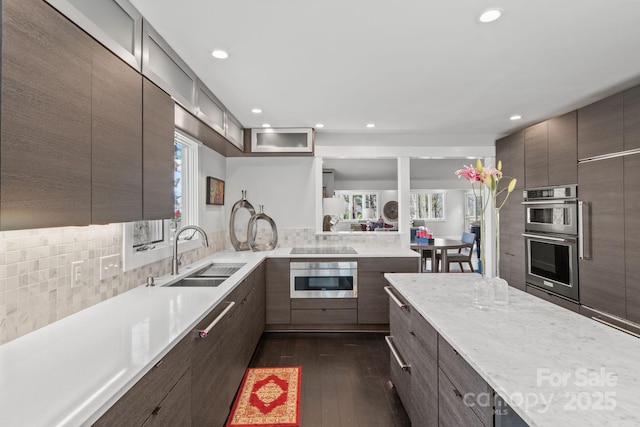 kitchen with light countertops, modern cabinets, stainless steel double oven, a sink, and dark wood-style floors