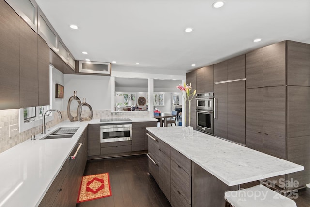 kitchen with a sink, a kitchen island, stainless steel double oven, modern cabinets, and dark wood-style floors