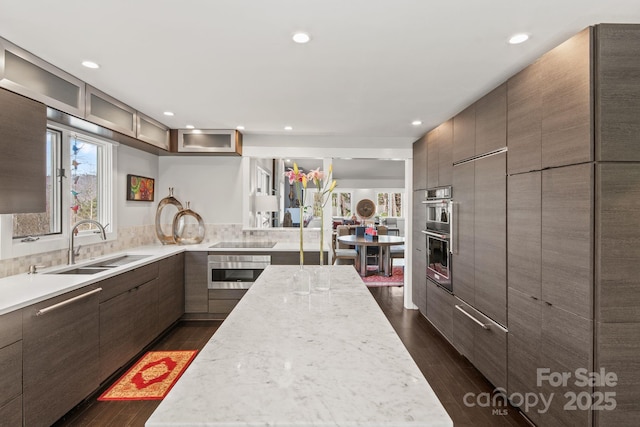 kitchen with a sink, modern cabinets, dark wood-style floors, glass insert cabinets, and black electric cooktop