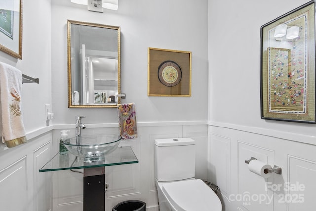 bathroom featuring a decorative wall, a sink, toilet, and wainscoting