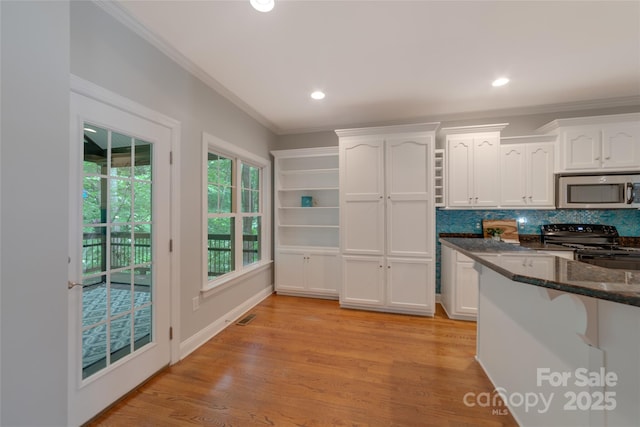 6414 Winding Creek Ln, Denver, NC 28037 - kitchen with stainless steel microwave, black range with electric cooktop, white cabinetry, dark stone countertops, and crown molding
