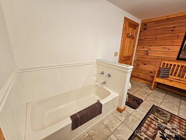 bathroom featuring wainscoting, toilet, and a bath