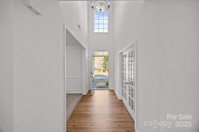 foyer featuring a wealth of natural light, a notable chandelier, wood finished floors, and a towering ceiling